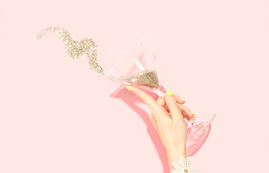 Woman with a martini glass throwing confetti on pink background